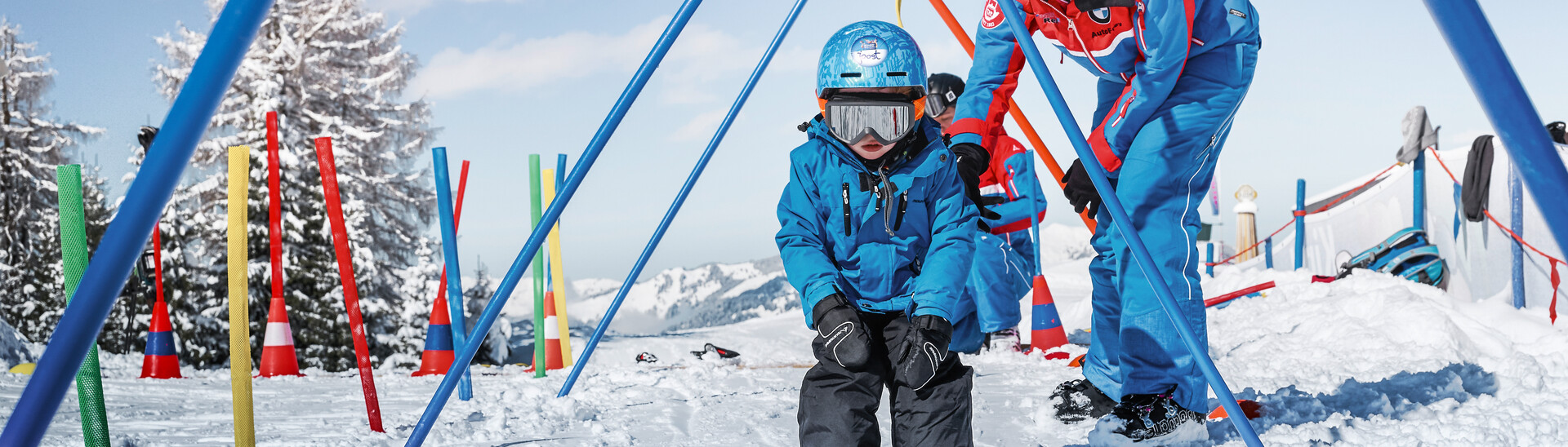 Kleiner Skifahrer fährt gemeinsam mit einem Skilehrer durch Übungsstangen im Kinderland Alpendorf im Skigebiet Snow Space Salzburg. | © Armin Walcher, Skischule Alpendorf