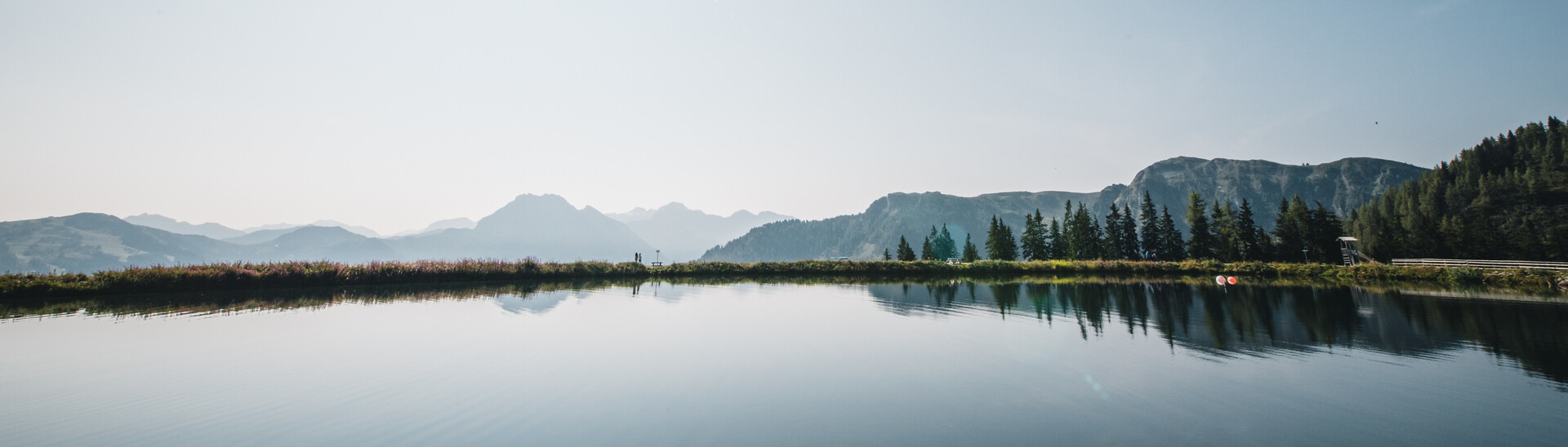 Soothing view of a crystal-clear mountain lake at Snow Space Salzburg under a bright blue sky with the sun at its zenith