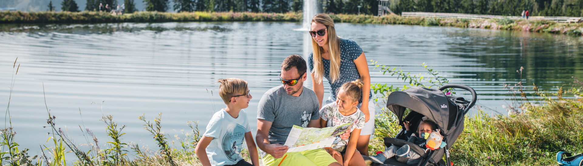 Family in front of a mountain lake orientating with a map in Snow Space Salzburg 